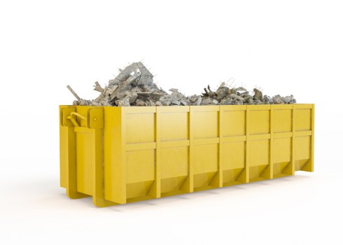 A large, rectangular, yellow skip container filled with a pile of mixed construction and demolition rubble, including broken concrete, bricks, and fragments of plaster. The skip is positioned on a white background, showing its sturdy metal sides with visible welds and rivets, and appears to be designed for waste collection and removal. The rubble is heaped unevenly, with some pieces spilling slightly over the top edge of the skip. The bright yellow colour of the skip contrasts with the predominantly grey and beige tones of the rubble material. The image reflects the type of waste collection services offered by Commercial Waste Southend on Sea, situated in Southend, with the skip likely placed in an outdoor setting such as a driveway or site area for efficient rubbish removal and disposal. The overall scene offers a clear and detailed visual representation of commercial waste management involving large skips used to handle significant debris loads, in line with services available in the local area.