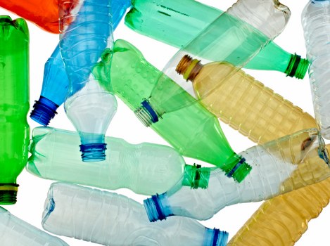 A collection of discarded plastic bottles in various colours, including green, blue, clear, and amber, scattered across a surface. The bottles are crumpled and partially flattened, with some caps missing or attached, and exhibit different textures from smooth to ridged. The background is bright and indistinct, emphasizing the focus on the waste plastic. This image highlights typical household or commercial waste collection items that a rubbish removal service such as Commercial Waste Southend on Sea might handle, with a particular focus on plastic waste within a local context such as Southend-on-Sea. The scattered bottles suggest an environment of refuse awaiting collection or disposal, relevant to professional rubbish removal operations in the area.